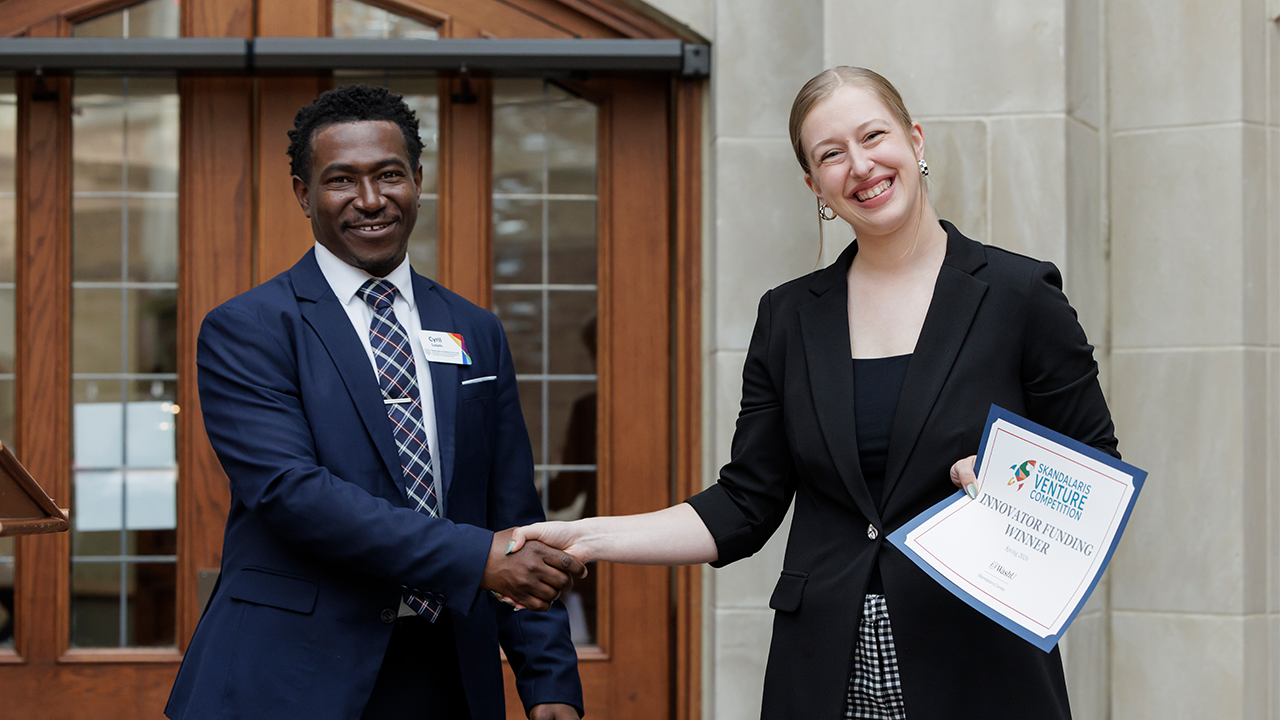 Two professionals shake hands outside a building; one holds an award certificate and smiles.