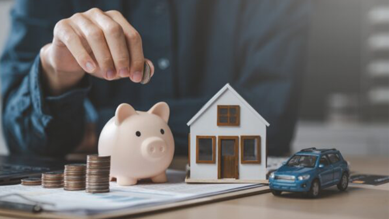 Person saving money for a home: piggy bank, miniature house, and car model with stacked coins on a document table