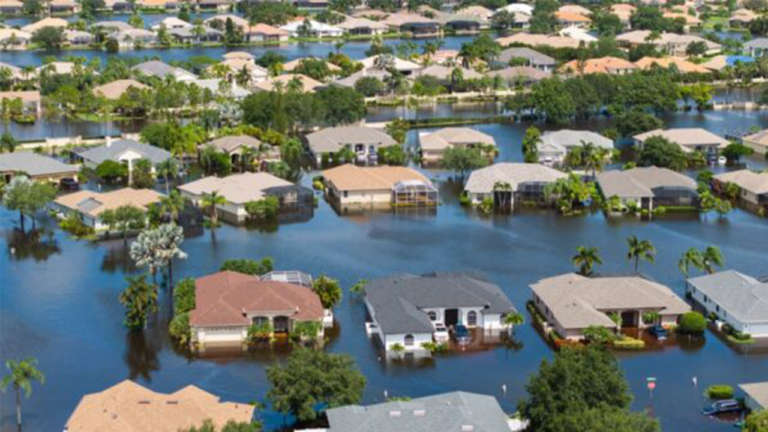 Submerged suburban neighborhood with floodwater surrounding yards and houses from an aerial view.