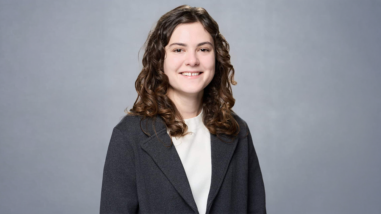 Smiling woman in a dark blazer and white blouse, posing for a professional headshot against a gray backdrop.