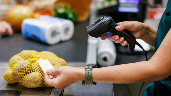 Cashier scans a bag of potatoes at the checkout with a handheld barcode scanner