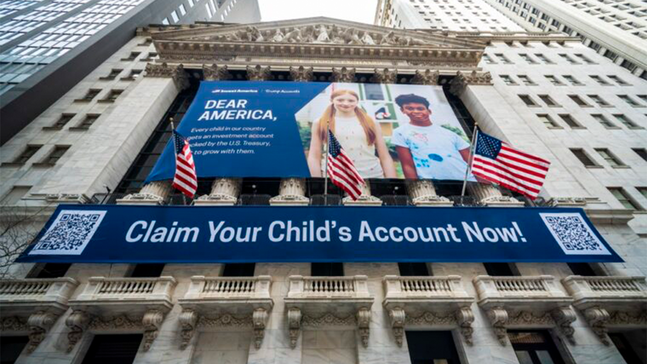 Large blue banner across a historic building reads 'Claim Your Child's Account Now!' with QR codes on both ends and American flags nearby, suggesting a campaign or advertisement.