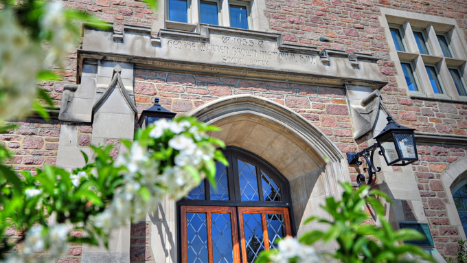 Entrance to a historic brick building with an arched stone doorway and vintage lanterns, framed by white flowering branches in the foreground.