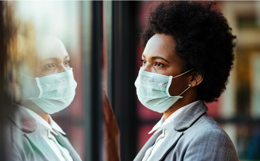 Image of Black person staring out the window while wearing a mask.