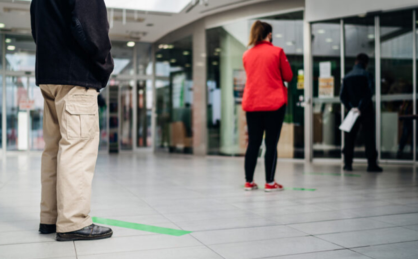 People in mall socially distanced, man standing behind green line