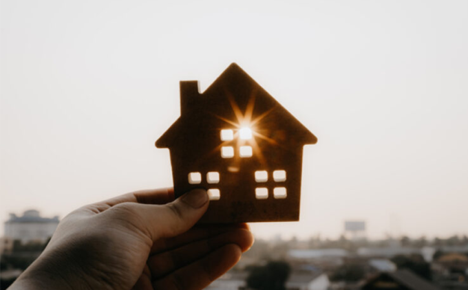 A hand holds a cut-out of a house up to the morning sun