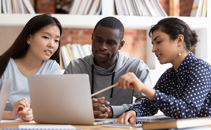 Diverse group of students in library around laptop having discussion