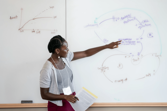 Teacher pointing at a dry erase board with a diagram.